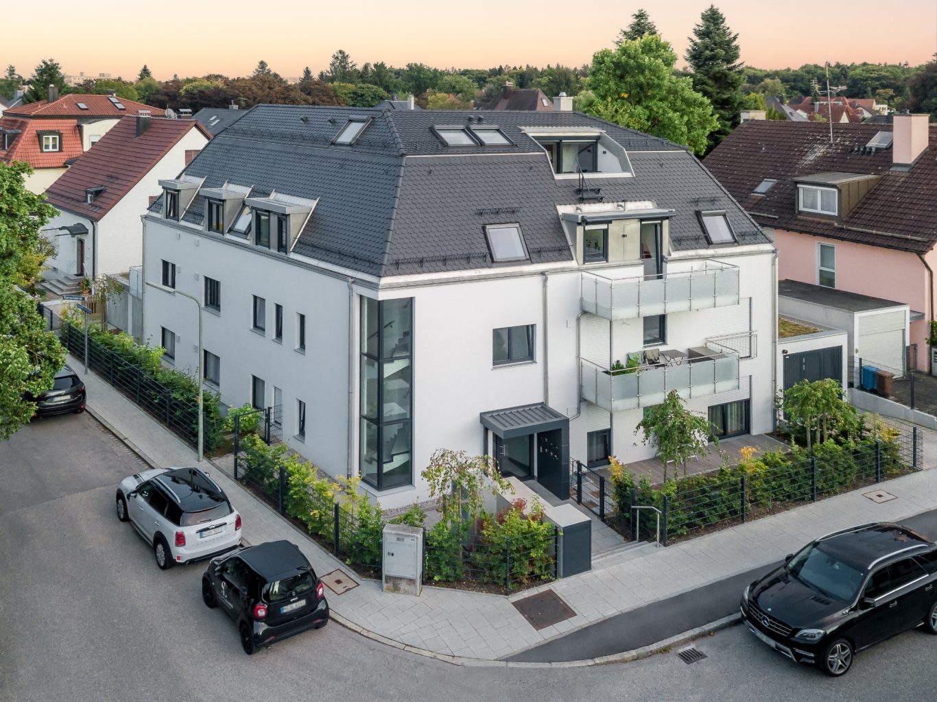 München - Großhadern Moderne, dreigeschossige Wohnanlage mit heller Fassade und grünen Pflanzen am Eingang.