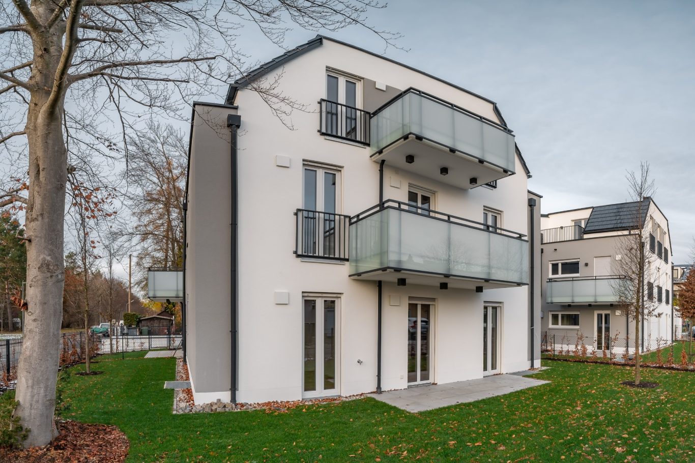Ottobrunn Modernes Wohngebäude mit Balkonen, umgeben von Rasen und Bäumen.