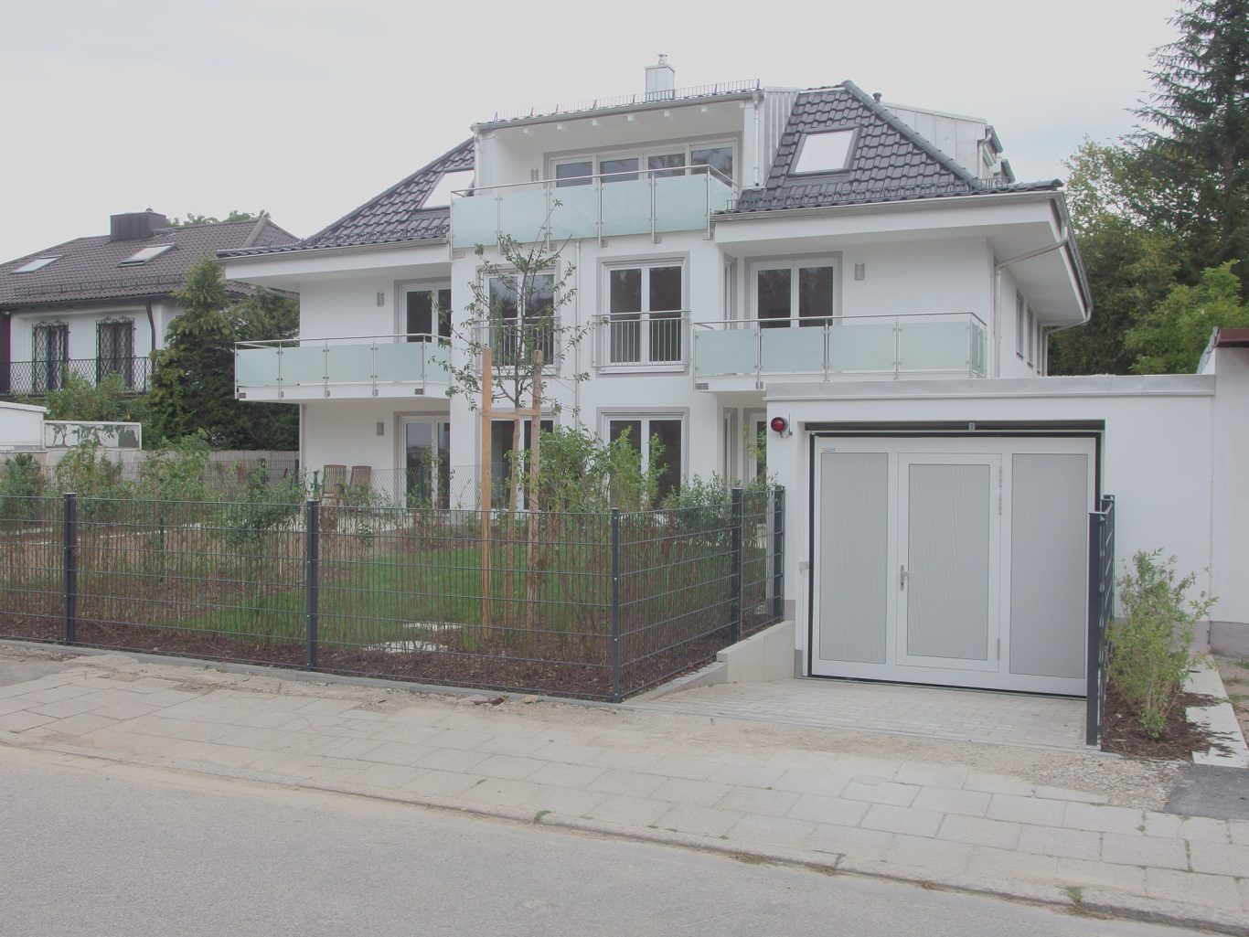 München - Großhadern Moderne, zweigeschossige Villa mit Garten und Zaun, gepflasterter Zufahrt.